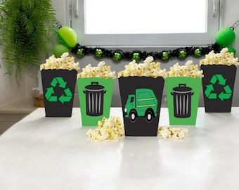 May include: Five black and green popcorn boxes with different designs. The designs include a recycling symbol, a garbage truck, and a trash can. The boxes are filled with popcorn.