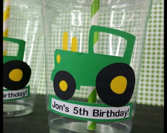 May include: Clear plastic cups with green and yellow tractor designs and the text "Jon's 5th Birthday!" printed on them. The cups are decorated with a green tractor with yellow wheels and a black tire.