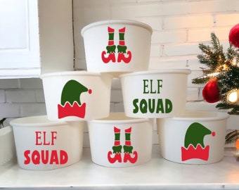 May include: Six white paper cups with festive Christmas elf designs. The cups feature green elf hats, red elf shoes, and the text "Elf Squad" in red letters.