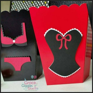 May include: Two red and black party favor boxes with a scalloped edge. One box has a black bra and panty cutout, the other has a black corset cutout with a red bow. The boxes have the text "Grace Giggles and Glue" on the bottom.