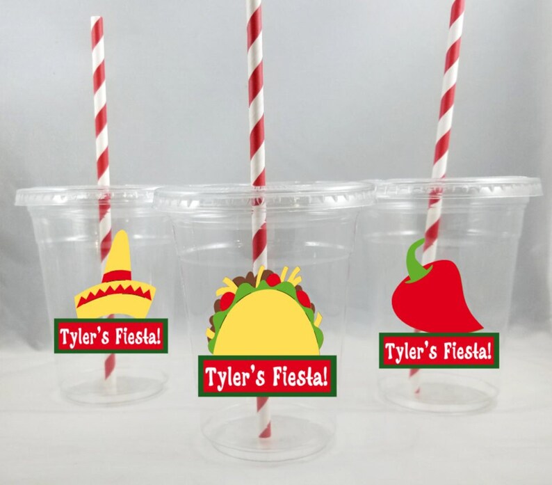K&ouml;nnte beinhalten: Drei durchsichtige Plastikbecher mit rot-wei&szlig; gestreiften Strohhalmen. Jeder Becher hat einen gr&uuml;n-wei&szlig;en Aufkleber mit dem Text "Tyler's Fiesta!" und ein anderes festliches Bild: einen Sombrero, einen Taco und eine rote Chilischote.