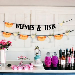 May include: A black banner featuring the text WEENIES & TINIS, decorated with alternating illustrations of hot dogs and martini glasses. A second, lower banner displays a repeating pattern of hot dogs and martini glasses on a string.
