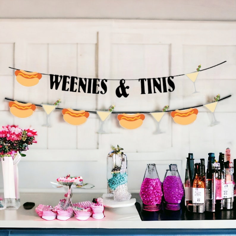 May include: A black banner featuring the text WEENIES & TINIS, decorated with alternating illustrations of hot dogs and martini glasses. A second, lower banner displays a repeating pattern of hot dogs and martini glasses on a string.