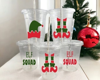 May include: Set of five clear plastic cups with festive Christmas elf designs. The cups have red and green elf hats, boots, and the text "Elf Squad".