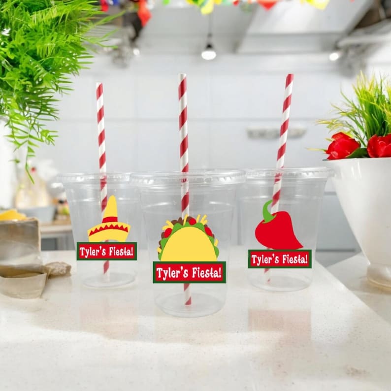 K&ouml;nnte beinhalten: Drei durchsichtige Plastikbecher mit rot-wei&szlig; gestreiften Strohhalmen. Jeder Becher hat einen festlichen Aufkleber mit einem anderen mexikanischen Design: einen Sombrero, einen Taco und eine Chilischote. Die Aufkleber zeigen auch den Text "Tyler's Fiesta!"