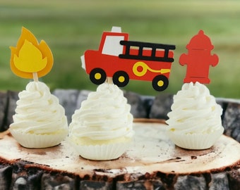 May include: Three cupcakes decorated with red, yellow and black firefighter themed toppers. The toppers are a fire engine, a fire hydrant and a flame.