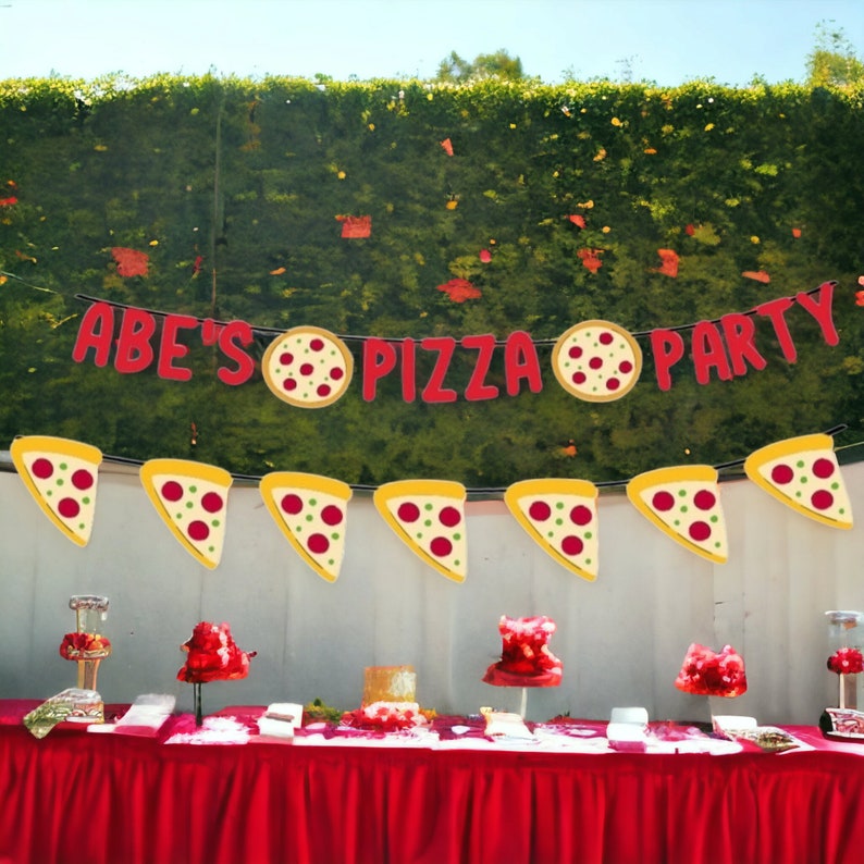 Puede incluir: Un banner de fiesta de pizza rojo y amarillo con el texto "Abe's Pizza Party". El banner est&aacute; decorado con rebanadas de pizza y pizzas enteras. Hay un mantel rojo con una variedad de comida en la mesa.