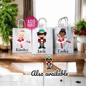 May include: Three white gift bags with handles, featuring Nutcracker and ballerina illustrations. The bags are personalized with the names Kinsley, Jack, and Tasha. The text "ADD NAMES!" is visible in the top left corner. A smaller Nutcracker illustration is shown below the bags with the text "Also available".