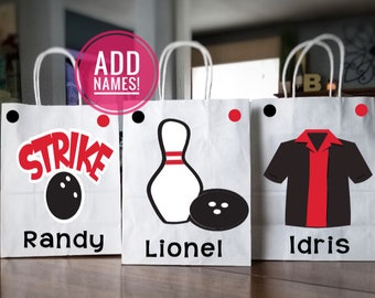 May include: Three white paper gift bags with red and black bowling-themed designs. The bags have black handles and are decorated with a bowling pin, bowling ball, and the word "Strike". The bags are labeled with the names "Randy", "Lionel", and "Idris".