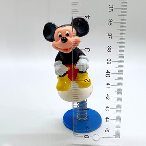 May include: A black and red Mickey Mouse figurine on a spring-loaded base. The base is white with a blue bottom. The figurine is about 4 inches tall.