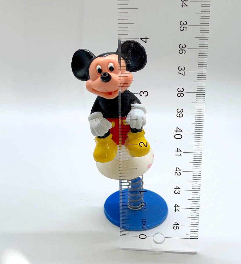 May include: A black and red Mickey Mouse figurine on a spring-loaded base. The base is white with a blue bottom. The figurine is about 4 inches tall.