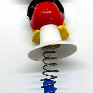 May include: A black and red Mickey Mouse character toy with a spring and blue base. The toy is made of plastic and has a yellow base.