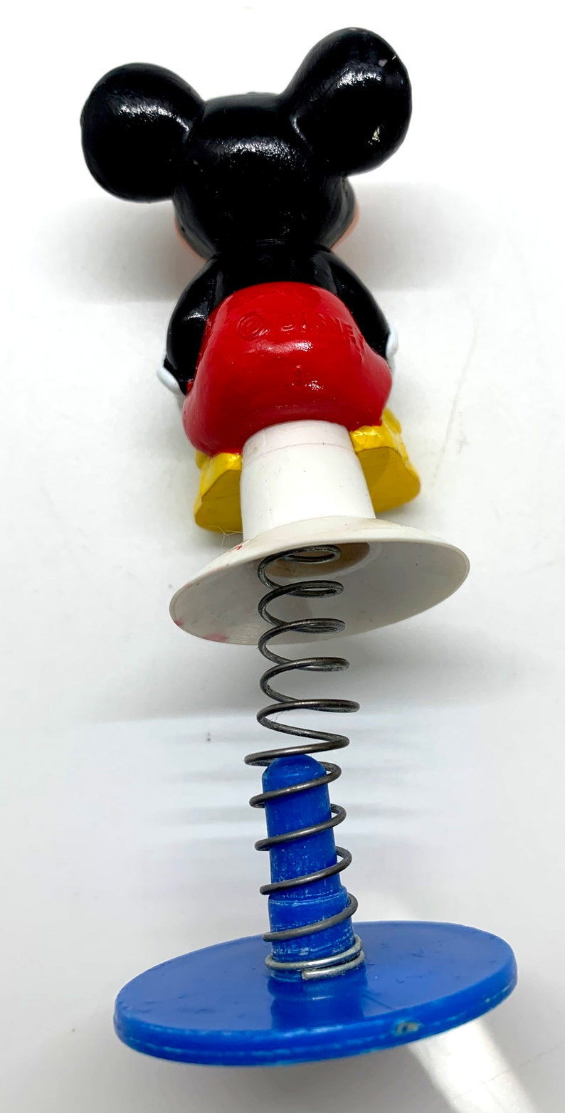 May include: A black and red Mickey Mouse character toy with a spring and blue base. The toy is made of plastic and has a yellow base.