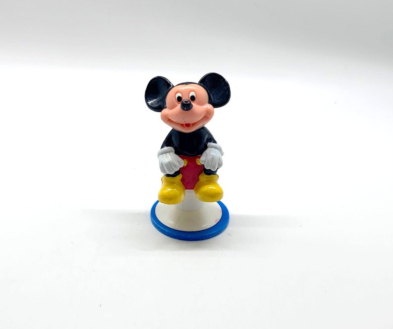 May include: A black and red Mickey Mouse figurine sitting on a white and blue base. The figurine is made of plastic and has a cartoonish style.