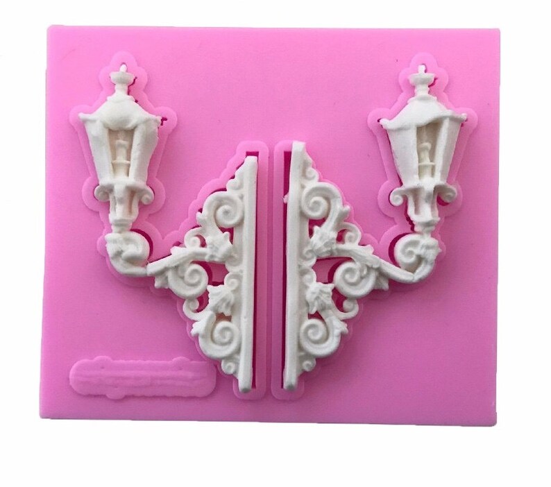 May include: A pink silicone mold for baking or crafting. The mold features two ornate lamppost designs with intricate details.