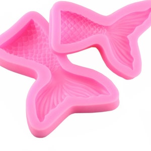 May include: Two pink silicone molds shaped like mermaid tails. The molds have a detailed scale pattern.