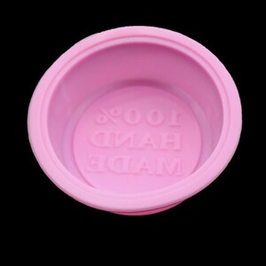 Puede incluir: Molde de silicona rosa con el texto "MADE HAND 100%" en relieve en la parte inferior.