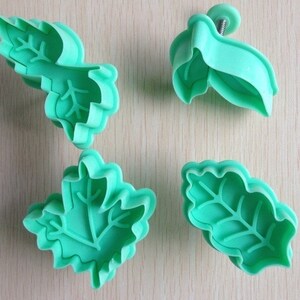 May include: Four green plastic leaf-shaped cookie cutters. The cutters are different sizes and shapes, with varying vein details. One cutter has a small handle with a screw.