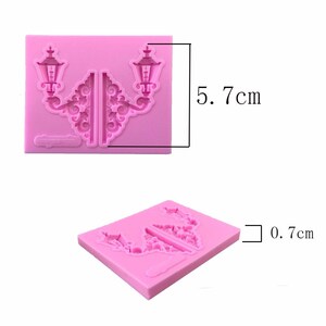 May include: Pink silicone mold for baking or crafting. The mold is shaped like two ornate street lamps with a decorative design. The mold measures 5.7 inches by 0.7 inches.