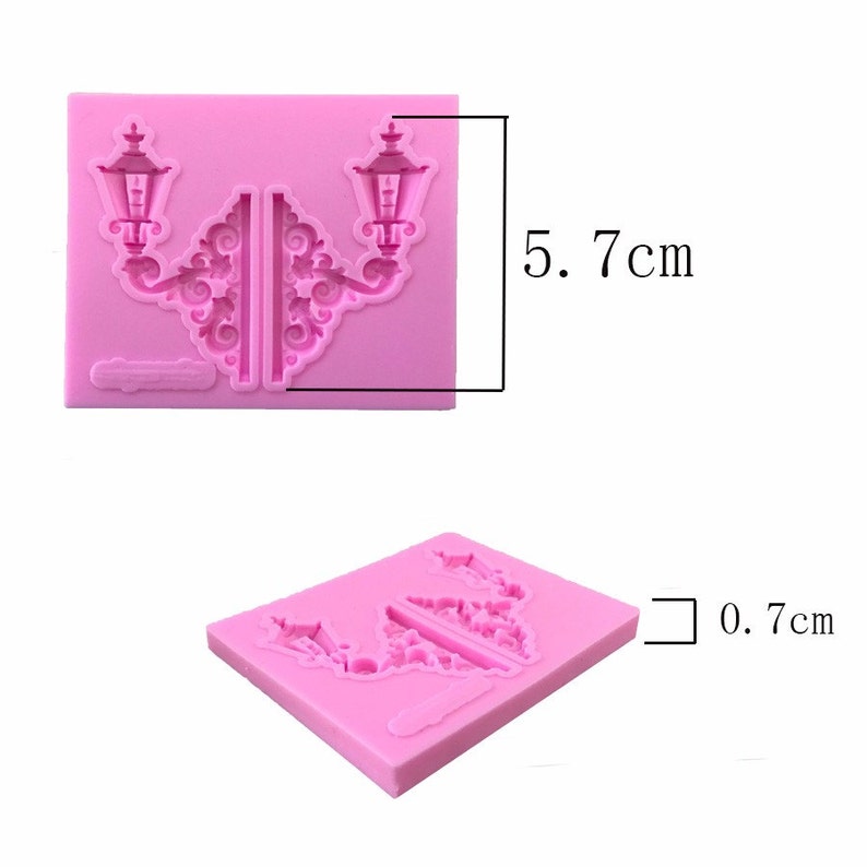 May include: Pink silicone mold for baking or crafting. The mold is shaped like two ornate street lamps with a decorative design. The mold measures 5.7 inches by 0.7 inches.
