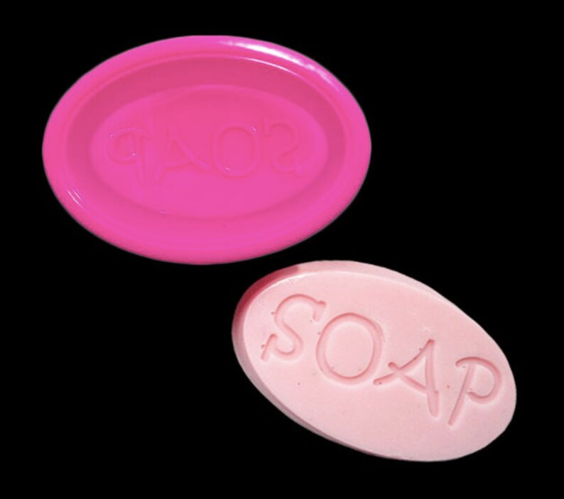 May include: A pink oval soap mold with the word "SOAP" embossed on it. Next to it is a pink oval bar of soap with the word "SOAP" embossed on it.