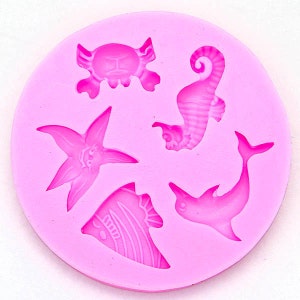 May include: Pink silicone mould with five different sea creature shapes: a crab, a starfish, a seahorse, a dolphin, and a fish. The mould is designed for making small, decorative items.