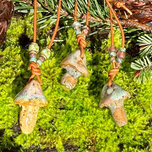 May include: Three ceramic mushroom pendants on brown leather cords with colourful beads. The mushrooms are glazed in shades of brown, green, and white.