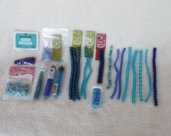 May include: Assortment of blue and turquoise seed beads, glass beads, and bead strands. The beads are packaged in small plastic bags and containers. The packaging includes the brand names "Lewiscrafts" and "Bead Gallery".