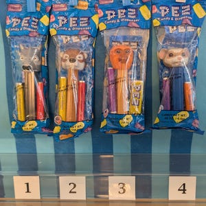 May include: Four PEZ candy and dispenser sets in original blue plastic packaging. Each set includes a character-topped dispenser and candy refills. The characters include a gray wolf, a brown squirrel, an orange monkey, and a tan hamster.