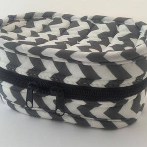 May include: A gray and white chevron patterned zippered pouch. The pouch is oval shaped and has a black zipper.