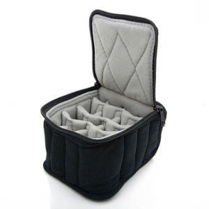 May include: Black, padded jewelry case with a gray interior. The case is open, revealing multiple compartments for organizing jewelry. The interior is lined with soft gray fabric. The case has a black zipper closure.