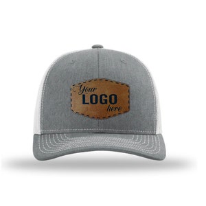 May include: Gray and white trucker hat with a brown leather patch that says "Your LOGO here" in navy blue lettering.