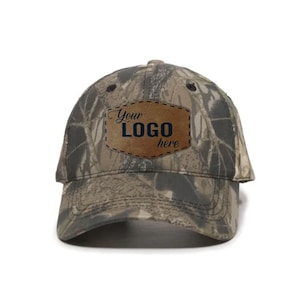 May include: Camouflage baseball cap with a curved brim. A brown leather patch on the front displays the text "Your LOGO here" in a dark blue color. The cap is designed with a classic six-panel construction.