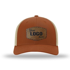May include: A brown and beige trucker hat with a brown leather patch that says "Your Logo here" in navy blue text.