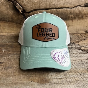 May include: A light blue and white trucker hat with a brown leather patch that says "The Four Legged Ranch".
