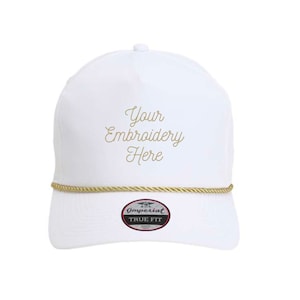May include: White baseball cap with gold rope detail and the text "Your Embroidery Here" in gold script. The cap has a curved brim and a "True Fit" label.