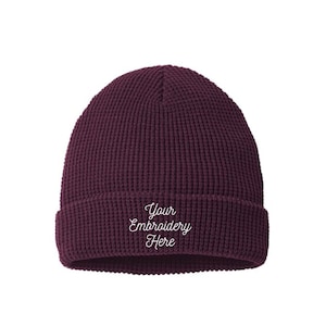 May include: A deep burgundy waffle-knit beanie with a folded cuff. The front of the cuff features the white embroidered text "Your Embroidery Here" in a cursive script font. The hat has a textured, grid-like pattern throughout the fabric.