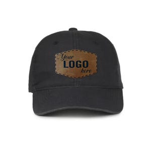 May include: Black baseball cap with a curved brim. A brown leather patch on the front displays the text "Your LOGO here" in a stylized font. The cap is made of a soft, durable fabric.