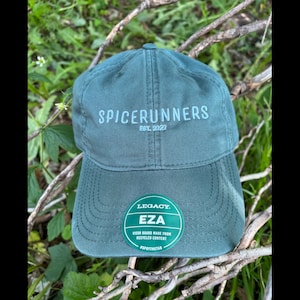 May include: A teal baseball cap with the text "SPICERUNNERS EST. 2022" embroidered on the front. A green sticker on the brim reads "LEGACY EZA VISOR BOARD MADE FROM RECYCLED CONTENT #SPOTTHETAB".