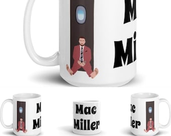 May include: White ceramic mug featuring a cartoon illustration of a person in a red suit sitting near a plane window. The mug also displays the name "Mac Miller" in bold black letters. A handle is on the left side.