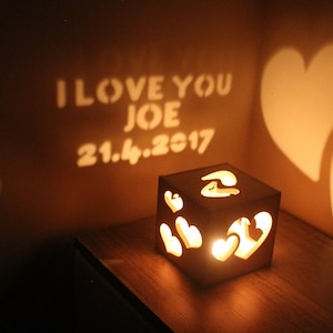 May include: A wooden box with a light inside casts a shadow on the wall that reads "I love you Joe 21.4.2017". The shadow also includes two hearts. The box has a heart-shaped design.