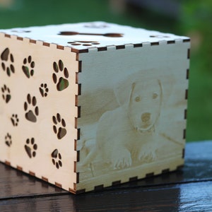 May include: A wooden box with a paw print design and a photo of a dog on the front. The box is light brown and has a natural wood finish.