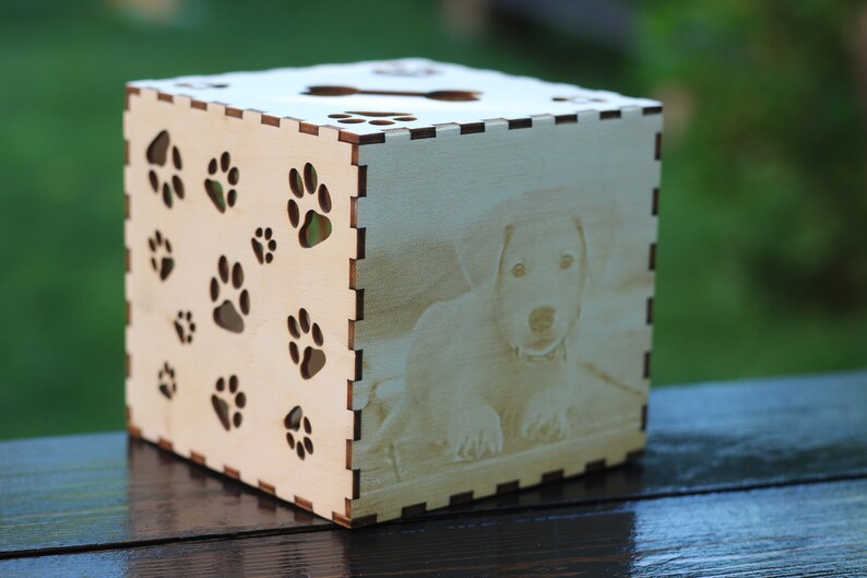 May include: A wooden box with a paw print design and a photo of a dog on the front. The box is light brown and has a natural wood finish.