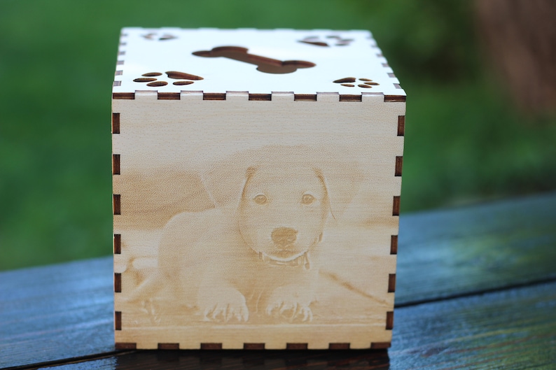 May include: A wooden tissue box with a laser-engraved image of a dog and paw prints. The top of the box has a cut-out bone shape.