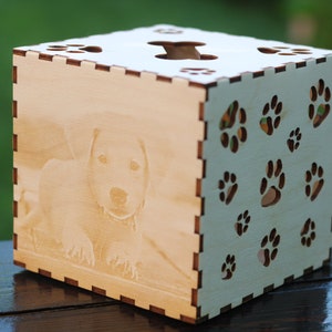 May include: A wooden box with a laser-engraved image of a dog and paw prints on the sides. The box is light brown and has a cutout in the top.