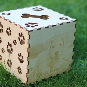 May include: A wooden box with a paw print design and a cutout of a bone on the top. The box has a photo of a dog on one side.