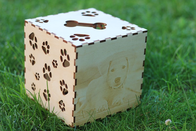 May include: A wooden box with a paw print design and a cutout of a bone on the top. The box has a photo of a dog on one side.
