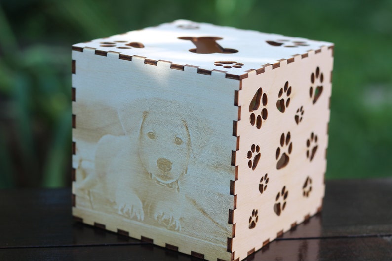 May include: A wooden tissue box with a cutout of a dog bone on the top and paw prints on the sides. The box has a photo of a dog on the front.