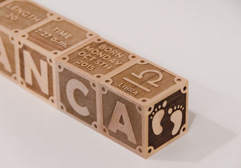 K&ouml;nnte beinhalten: Holzw&uuml;rfel mit gravierten Buchstaben, die "CANCA" buchstabieren, und Details zur Geburt eines Babys, einschlie&szlig;lich Datum, Uhrzeit, Wochentag und Sternzeichen Waage.