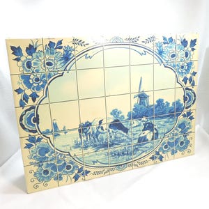 May include: A rectangular tile panel featuring a Dutch landscape scene. The panel is composed of multiple square tiles with a cream background and blue floral border. The central image depicts a windmill, cows, and a waterway.